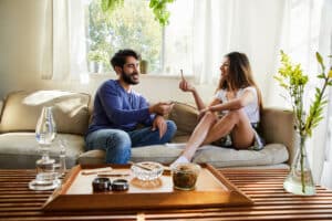 Young couple talking and smoking a joint together while sitting on their living room sofa at home