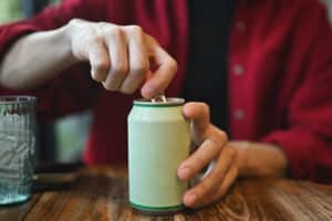 Close up with a Young Asian man's hands opening a drinking can while sitting at the wooden table.