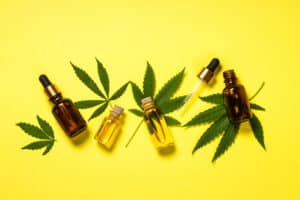 Cannabis oil in the bottle hemp oil with fresh cannabis leaves at yellow table. Top view with copy space.